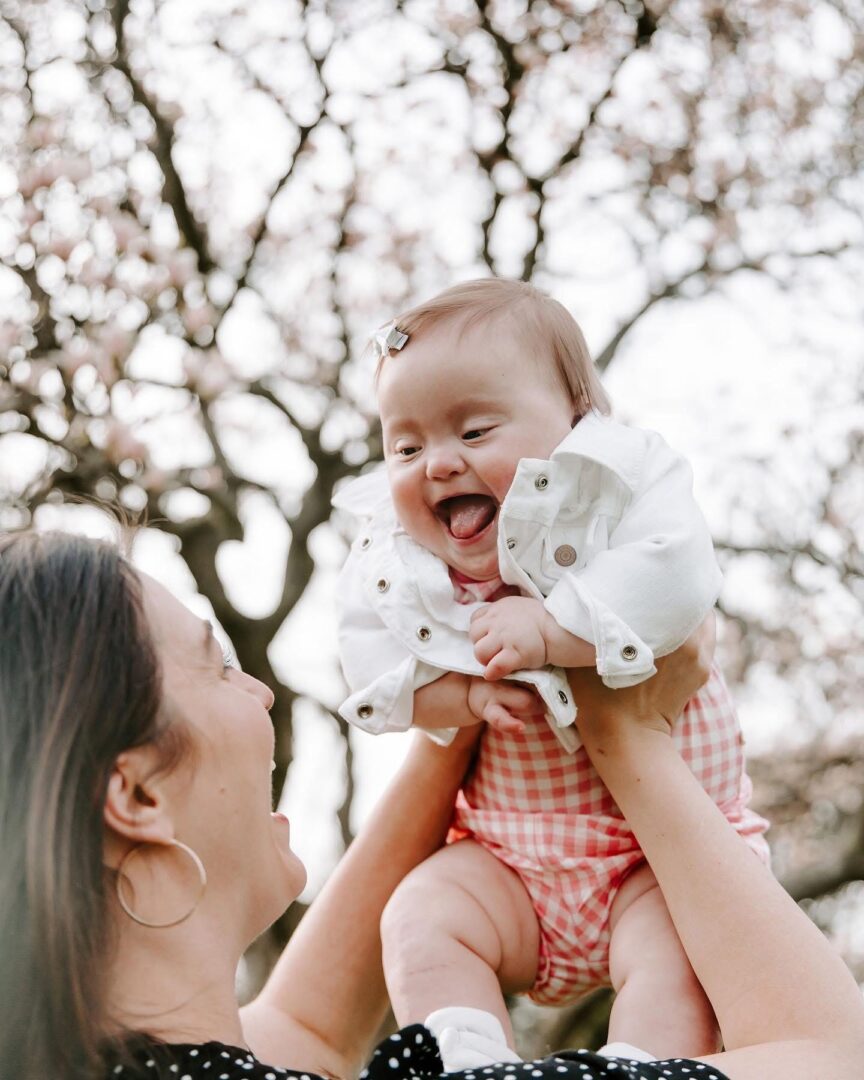 Jess holding Adeline up high with a big smile and joy. Down Syndrome does not get in the way of love and joy!