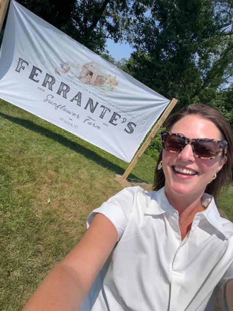 Photo of Jessica Quarello, our brand communications manager, posing near the sign to Ferrante's Sunflower Farm.